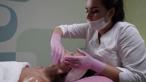Kosmetolog robi masaż podpoliczkowy twarzy atrakcyjnej kobiecie. — Wideo stockowe
