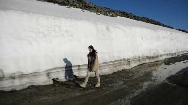Темноволосая девушка движется вдоль снежной стены в горах, оглядываясь вокруг — стоковое видео