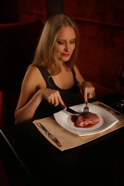 Blonde girl who smiles eats raw meat lying on her plate in a restaurant. — Stock Photo, Image