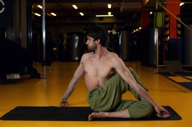 Yoga hocası Bharadvajasans 'ta oturur ve karanlık bir spor salonunda poz verir.
