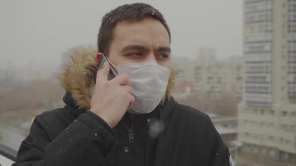 Человек в маске говорит по телефону на заднем плане города — стоковое видео