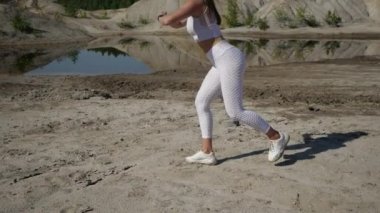 Beyaz takım elbiseli bir kız, taş ocağında denize karşı antrenman yapıyor.