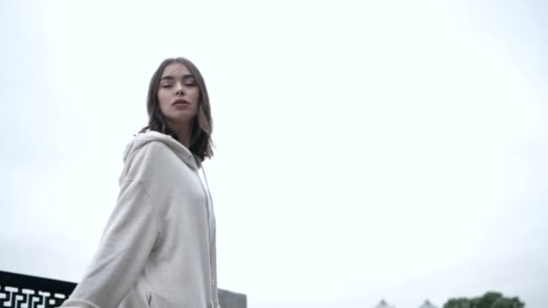 A young woman in a white hoodie walks along the embankment in the early morning — Stock Video