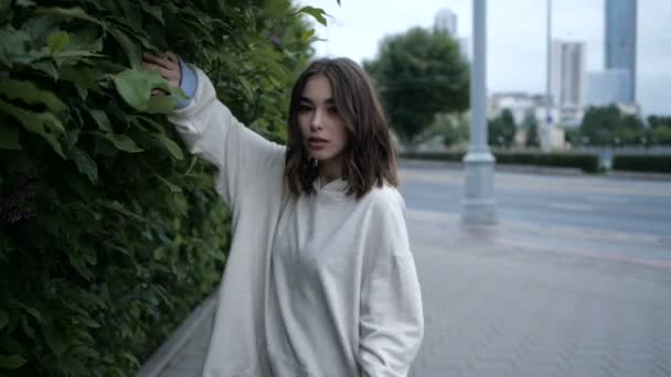 Cute girl walks near the green fence against the backdrop of the cityscape — Stock Video