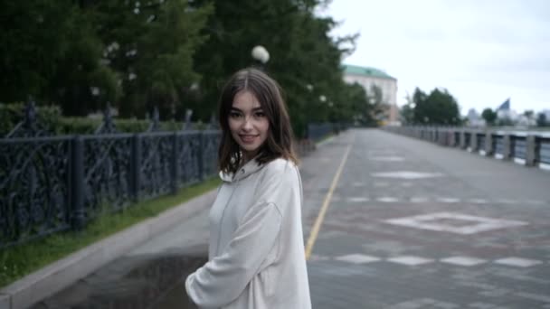 Smiling girl in a white hoodie, walks along the river embankment — Stock Video