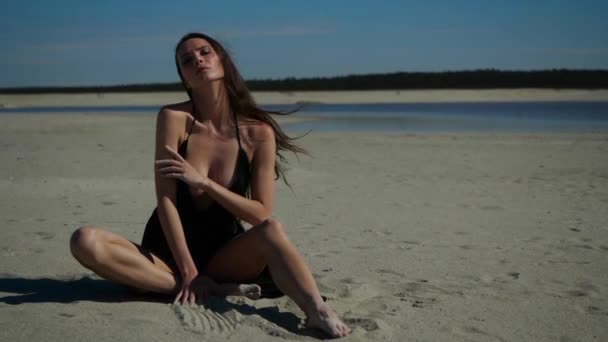 Joven morena sexy con un gran escote mira a la cámara en la playa — Vídeo de stock