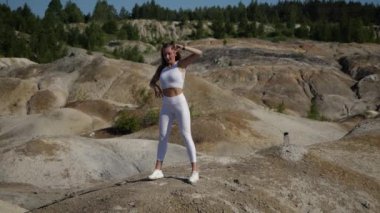 Genç bir kadın kumla çevrili açık havada çömeliyor.