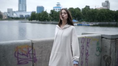 Beyaz kapüşonlu bir kız nehir kenarında yürüyor.