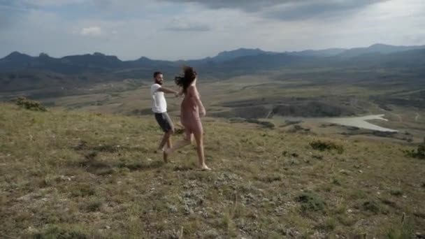 Det lyckliga paret håller varandra i handen, springer längs en slätt under den mulna himlen — Stockvideo