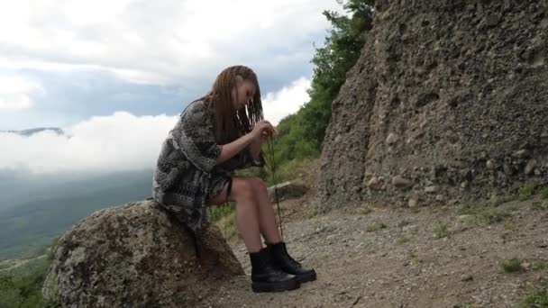 Ein Mädchen in einem grauen Umhang sitzt auf einem Stein und bindet ihre Schnürsenkel — Stockvideo