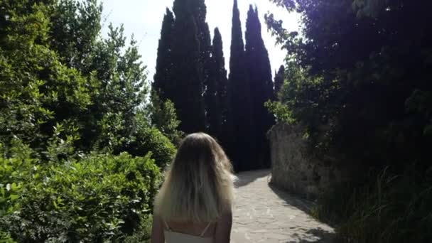 Slender girl in white, short dress enters a maze of greenery. — Stock Video