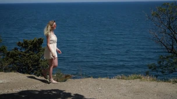 Una mujer hace un paseo a lo largo de la costa del mar disfrutando de los rayos del sol — Vídeos de Stock