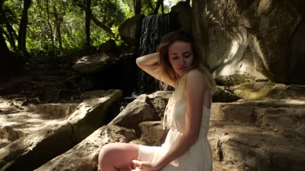 Cute blonde girl in white dress next to waterfall — Stock Video