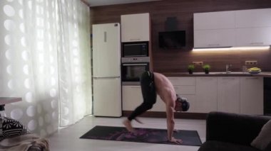 Çıplak gövdeli bir sporcu bacaklarını kendine doğru çeker ve zıplar.