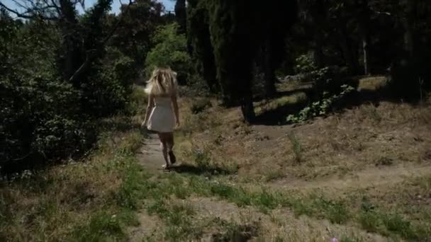 白いショートドレスの女性が背の高い山から道を走っていく — ストック動画