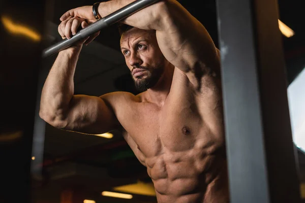 Spor fiziği olan vücut geliştirici turnikeye yaslanan kamera için poz verir.
