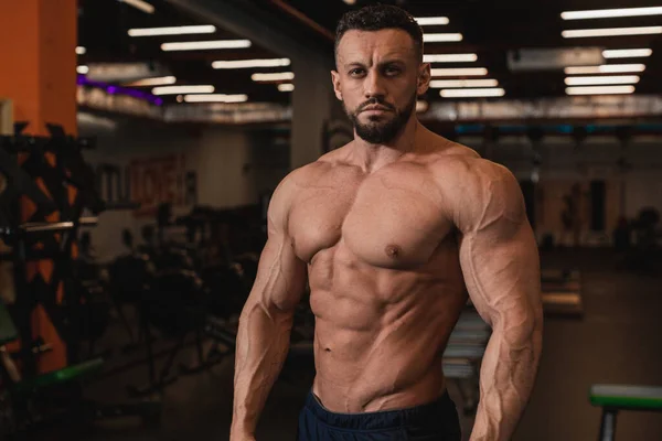 Spor salonunun arka planında çıplak gövdeli esmer bir erkek.