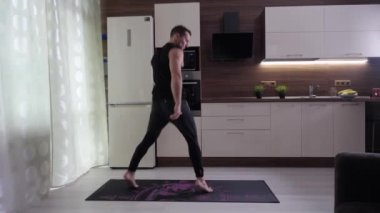 Sporcu ev mutfağında, ayakları ve kalçaları üzerinde egzersiz yapar.