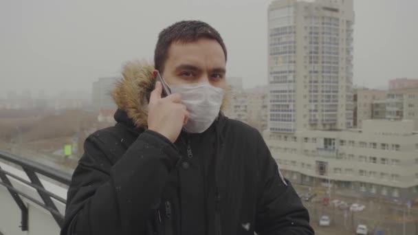 Homme dans un masque médical parle sérieusement au téléphone paysage urbain en arrière-plan — Video