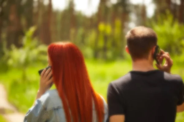 Blurry background of a young couple on a walk talking on smartphones. Rear view of two people with phones. Phone addict concepts. Telephone addiction.