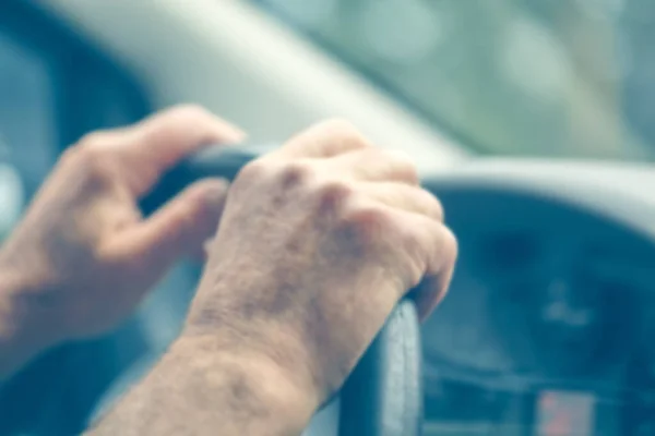 Defocused background of the driver\'s hand with blue toning. Male hands on the steering wheel driving a car Driving a car. Transport, vacation, travel and automotive concept.