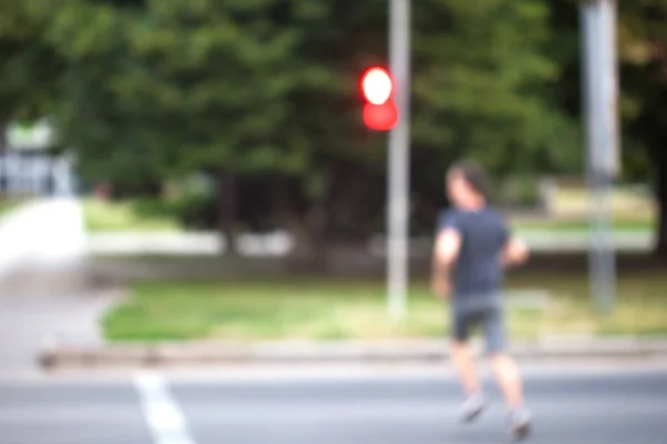 Blurred background. A man runs across the street at a red traffic light. After the signal turns red, the pedestrian crosses the road. A pedestrian violates traffic rules.
