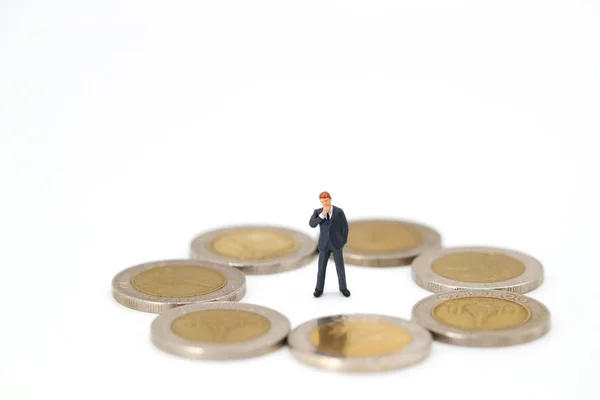 Personas en miniatura: hombre de negocios mirando alrededor de las monedas y pensando algo (concepto de competencia financiera y empresarial — Foto de Stock