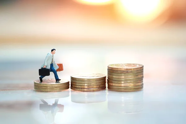 Miniature people: businessman walking or running to the top of stacking golden coins with sun light and reflection (Financial and Business growth concept) — Stock Photo, Image