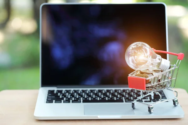 Carro y monedas con bombilla de vidrio eléctrica en el ordenador, idea para ir de compras y pago en línea utilizando como fondo de negocios —  Fotos de Stock