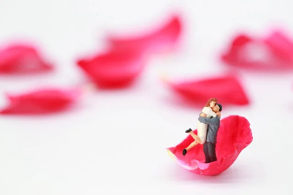 Miniature people: a couple standing on red rose petal on white background, idea for love and valentines day — Stock Photo, Image