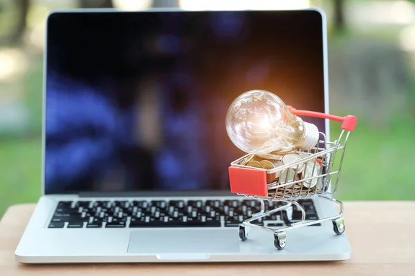 Carro y monedas con bombilla de vidrio eléctrica en el ordenador, idea para ir de compras y pago en línea utilizando como fondo de negocios —  Fotos de Stock