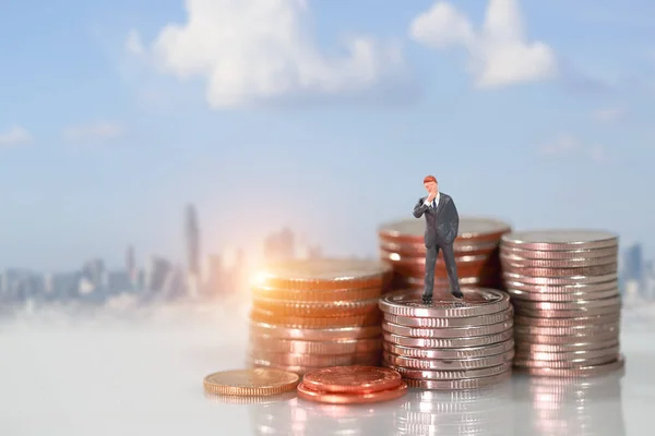 Miniaturmenschen: Geschäftsmann steht auf einem Podium zum Münzstapeln mit unscharfem Hintergrund (dieses Bild für das Konzept des finanziellen und geschäftlichen Wettbewerbs — Stockfoto
