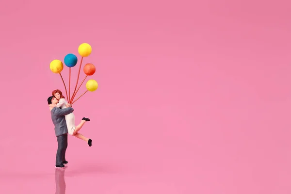 Миниатюрные люди: пара, стоящая и держащая воздушный шар на розовом фоне, идея концепции любви — стоковое фото