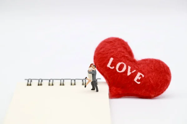 Miniature people: a couple standing on notebook with read heart symbol, idea for valentine background — Stock Photo, Image