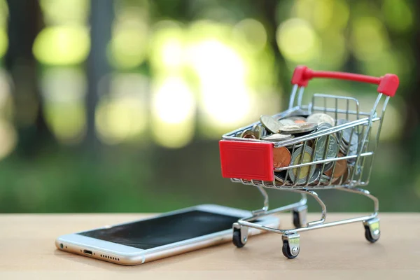 Carrinho com moedas e telefone celular em madeira, ideia para compras e pagamento on-line usando como plano de fundo de negócios — Fotografia de Stock