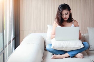 rahat bir günde oturma odasında beyaz yelek ve mavi jean ile bilgisayar kullanarak güzel kadın portre