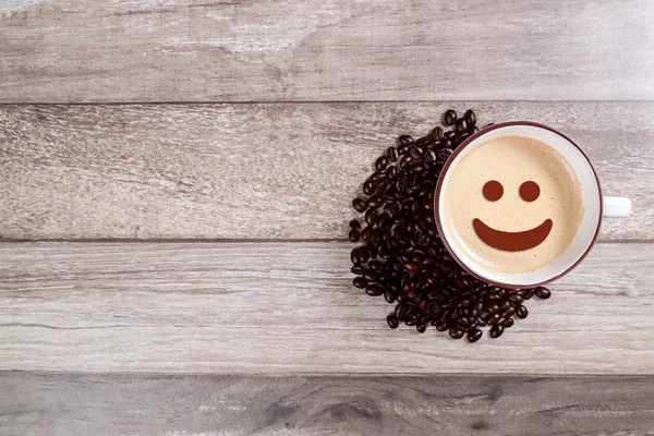 Tazza di caffè con viso sorridente e fagiolo sul tavolo di legno — Foto Stock