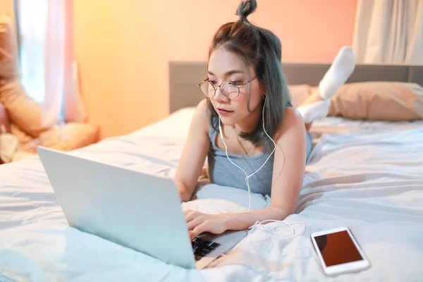 Hermosa y sexy mujer usando ordenador portátil y escuchar música desde el teléfono celular en la cama —  Fotos de Stock