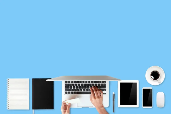 Pracovní stůl s ručičky na přenosném počítači, kreditní kartu, šálek kávy a mobilní telefon na modrém pozadí (nebo koncept nakupování a placení on-line) — Stock fotografie