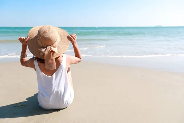 Vista posterior retrato de sexy chica joven asiática en bikini y sombrero, mirando hacia la playa tropical mientras está sentado en la playa de arena en la naturaleza con cielo azul . — Foto de Stock