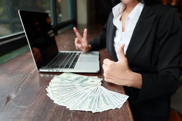 Бізнес-леді показує великий палець і символ перемоги на руках для сенсу успіху проекту з банкнотами і комп'ютером на столі — стокове фото