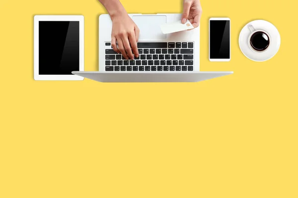 Technology working table with woman hands on laptop computer, credit card, coffee cup and cell phone on yellow background (or shopping and payment online concept) — Stock Photo, Image