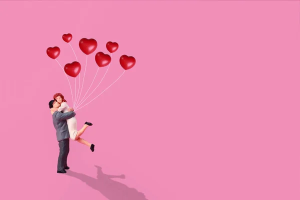 Miniatur-Paar steht und hält roten Liebesballon vor rosa Hintergrund — Stockfoto