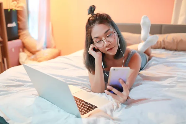 Hermosa y sexy mujer usando ordenador portátil y escuchar música desde el teléfono celular en la cama —  Fotos de Stock