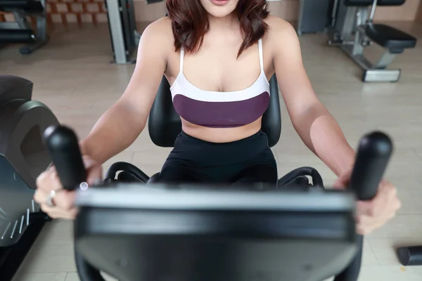 Porträtt av ung frisk och sportig kvinna med hjälp av träningsmaskin i gymmet (denna bild för fitness och träning koncept) — Stockfoto