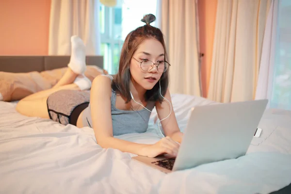 Красива і сексуальна жінка використовує ноутбук і слухає музику з мобільного телефону на ліжку — стокове фото