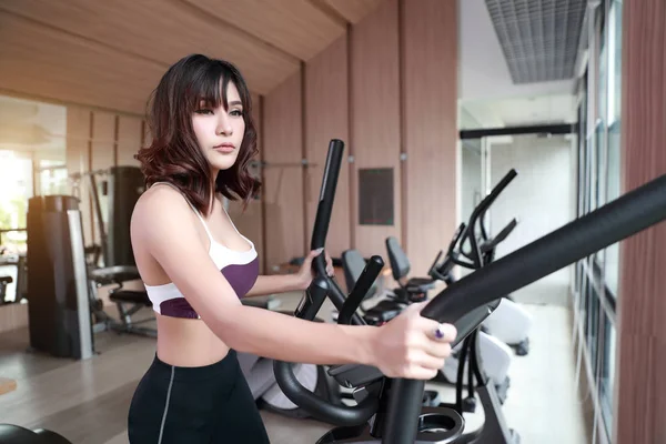 Retrato de jovem mulher saudável e desportiva usando máquina de exercício no ginásio (esta imagem para fitness e conceito de treino ) — Fotografia de Stock