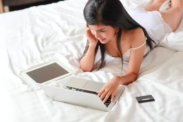 Hermosa y sexy mujer de compras y pago en línea mediante el uso de la computadora y la tableta en el dormitorio con tarjeta de crédito —  Fotos de Stock