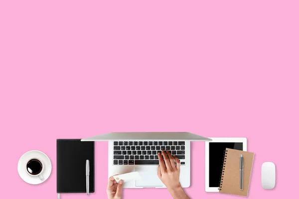 Technologia stół roboczy z rąk kobieta na laptopie komputera, karty kredytowej, filiżankę kawy i telefon komórkowy na różowe tło (lub zakupy i płatności koncepcji online) — Zdjęcie stockowe