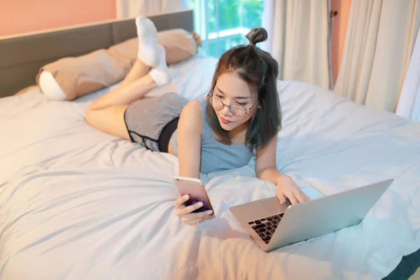 Hermosa y sexy mujer usando ordenador portátil y teléfono celular antes de ir a dormir —  Fotos de Stock